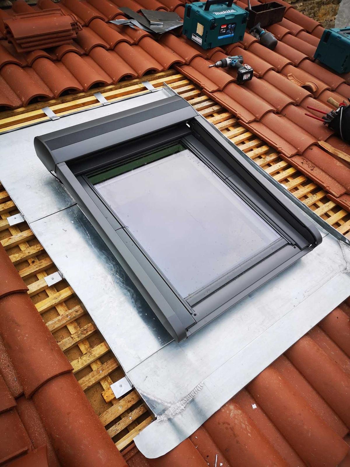 Pose de fenêtre de toit Velux avec volet roulant sur toiture en tuiles